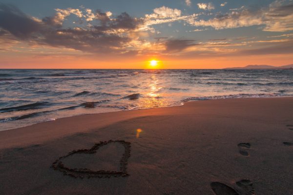 coeur dessiné sur le sable en bord de mer avec un soleil couchant